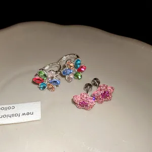 Close-up of colorful rhinestone flower hoop earrings and pink star studs on a dish