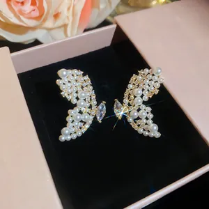 Boucles d'oreilles papillon élégantes avec perles et cristaux dans une boîte à bijoux rose.