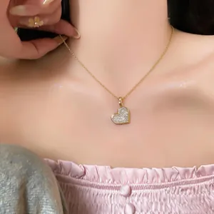 Nahaufnahme einer eleganten Goldkette mit einem funkelnden Herzanhänger aus Zirkonia auf Haut.
