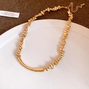 Detail view of a gold-toned necklace with irregular beads and a curved bar design.
