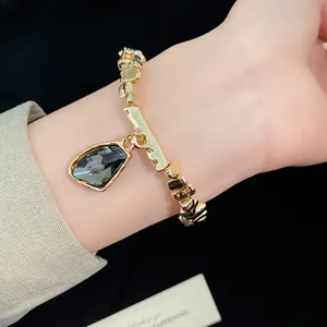 Detailed view of irregular gold bracelet with dark grey geometric gem pendant