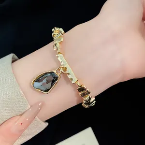 Close-up of a gold bracelet with a dark faceted irregular gemstone pendant