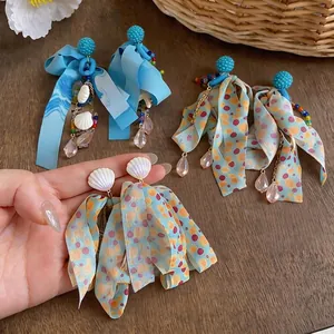 Orecchini a fiocco in chiffon con conchiglie e nappe di perline su tavolo in legno