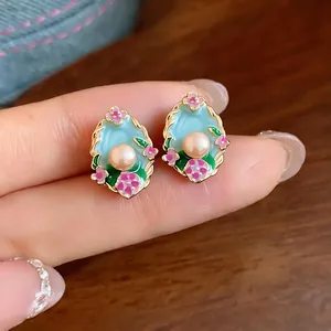 Dettaglio di orecchini a perla ovali con smalto azzurro e motivi floreali rosa