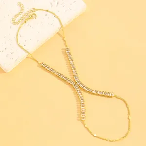 Gros plan d'une chaîne de main dorée avec un élégant motif en X en strass baguette.