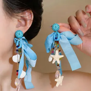 Dettaglio di orecchini a fiocco in chiffon blu con pendenti a conchiglia e stella marina
