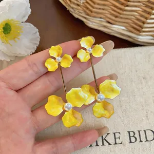 A detailed close-up of yellow enamel flower earrings featuring elegant pearl centers
