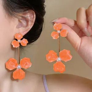 Detailed macro view of vibrant orange enamel flower pendant earrings with pearl centers.