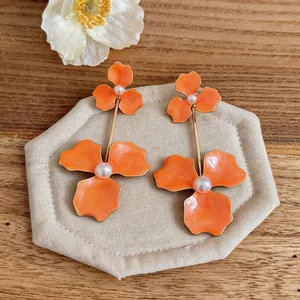 Close-up of exaggerated orange dripping oil flower earrings with elegant pearl details.
