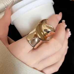 Close-up of golden irregular twisted metal ring worn on hand holding a white coffee cup