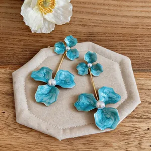 Close-up detail of elegant blue enamel flower earrings with pearls and a golden stem.