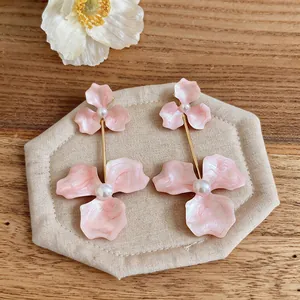 Detailed view of pink floral drop earrings with pearl accents on a wooden background
