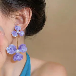 Macro view of elegant purple oil-dripping floral drop earrings with pearls on female model