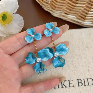 Detailed macro view of oversized blue enamel flower drop earrings with white pearl accents