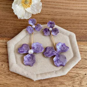 Close-up detail of oversized purple enamel flower earrings with pearl accents on display.