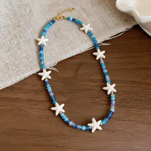 Close-up van blauwe glaskralen en witte zeesterren op een ketting in oceaanstijl