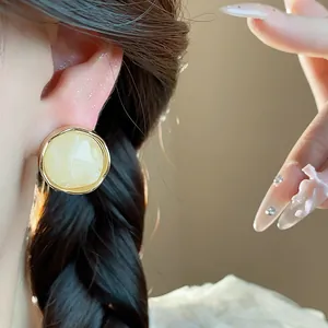 Close-up detail of a vintage cream resin stud earring with gold-tone border on model's ear