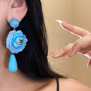 Primo piano di eleganti orecchini a pendente con fiore di resina blu e goccia d'acqua