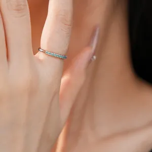 Macro view of a slim silver ring featuring small blue zircon stones on a model's finger