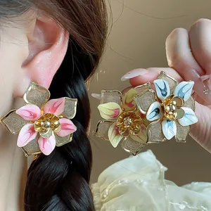 Close-up of elegant enamel flower stud earrings with delicate metallic mesh petals.
