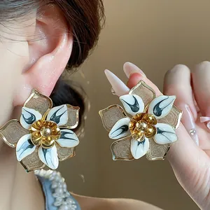 Close-up of vintage oversized enamel flower stud earrings with gold and white detailing.