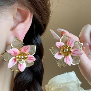 Detailed view of oversized pink enamel flower stud earrings with gold accents