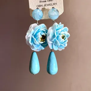 Primo piano dettagliato di eleganti orecchini a fiore in resina blu con pendenti goccia.