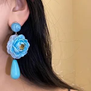 Dettaglio di orecchini a fiore in resina blu indossati sull'orecchio di una modella asiatica.