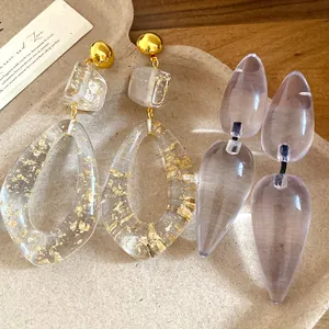Detailed view of lavender translucent resin and gold leaf teardrop earrings on a beige tray
