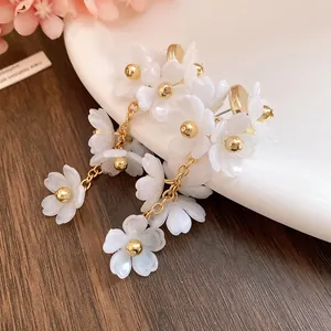 Close-up of white acrylic flower tassel earrings with elegant gold chain details.