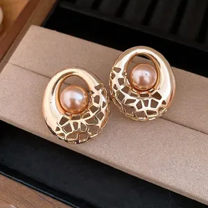 Élégantes boucles d'oreilles rondes dorées ajourées avec perles roses centrales sur présentoir.