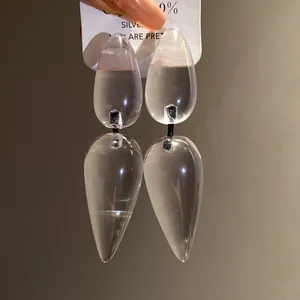 Close-up of transparent resin water-drop earrings with clear texture and silver needle.