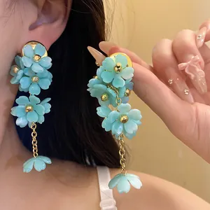 Close-up of elegant light blue acrylic flower tassel earrings with gold chain detail