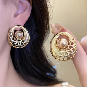 Gros plan de boucles d'oreilles dorées évidées avec perle sur un mannequin.