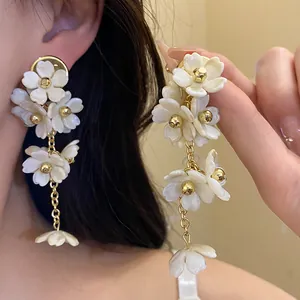 Detail of white acrylic flower tassel earrings with gold-tone hardware on model
