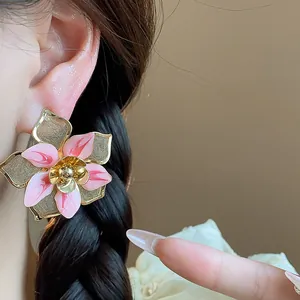 Detailed close-up showing a large pink enamel flower stud earring worn on an ear