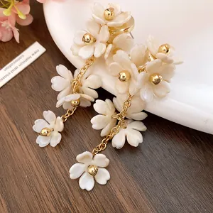 Elegant white acrylic flower tassel earrings with gold accents on a soft background.