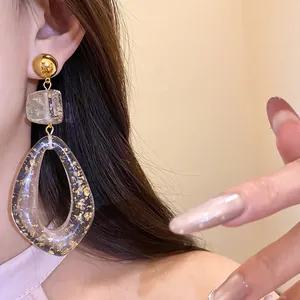 Close-up of stylish oversized resin drop earrings with gold flakes on a model's ear