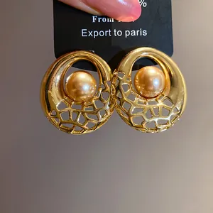 Gros plan d'élégantes boucles d'oreilles dorées évidées avec perle champagne