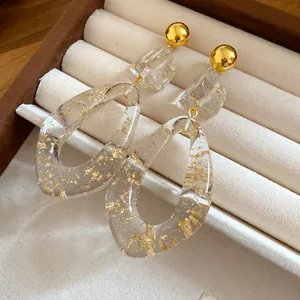 Close-up of teardrop resin earrings with gold leaf inclusions on a beige display tray.