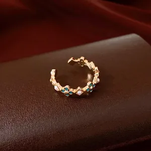 Elegant gold open ring featuring blue flower motifs and small white pearls on a leather base.