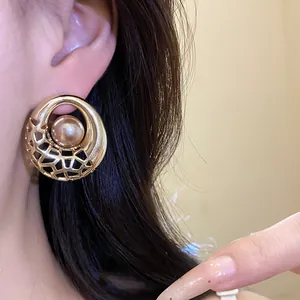 Vue détaillée de boucles d'oreilles dorées ajourées avec une perle centrale sur l'oreille