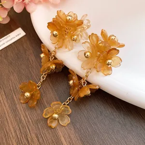 Close-up of amber acrylic flower tassel earrings with golden chains on white plate