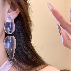 Close-up detail of stylish clear resin water drop pendant earrings on a model's ear