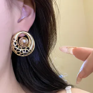 Vue détaillée d'une boucle d'oreille ajourée dorée avec une perle de champagne centrale