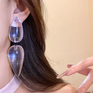 Detailed view of large transparent resin teardrop dangling earrings worn on a model's ear