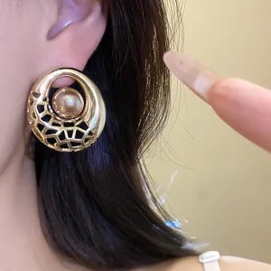 Gros plan détaillé de boucles d'oreilles dorées rondes évidées avec une perle centrale
