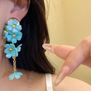 Detail shot of elegant teal acrylic flower tassel earrings with golden chains.