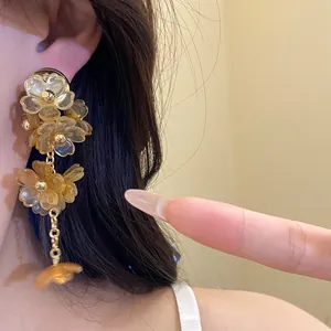 Macro view of elegant amber acrylic flower tassel earrings showing the delicate wearing effect