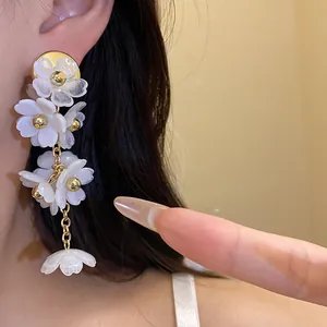 Detail view of white acrylic flower tassel earrings with gold centers on model ear.